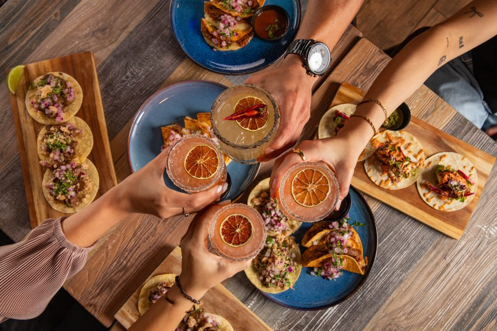 Friends toasting margaritas over a table of tacos